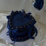 Heart-shaped dark blue cake with gold pearls and ribbons on white satin.