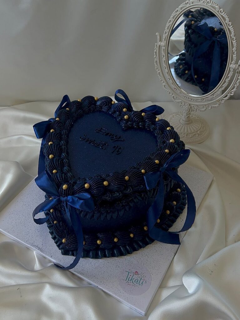 Heart-shaped dark blue cake with gold pearls and ribbons on white satin.