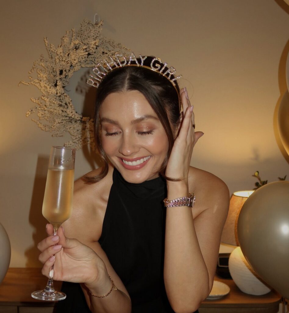 Woman in a black halter dress and birthday headband holding a champagne glass.