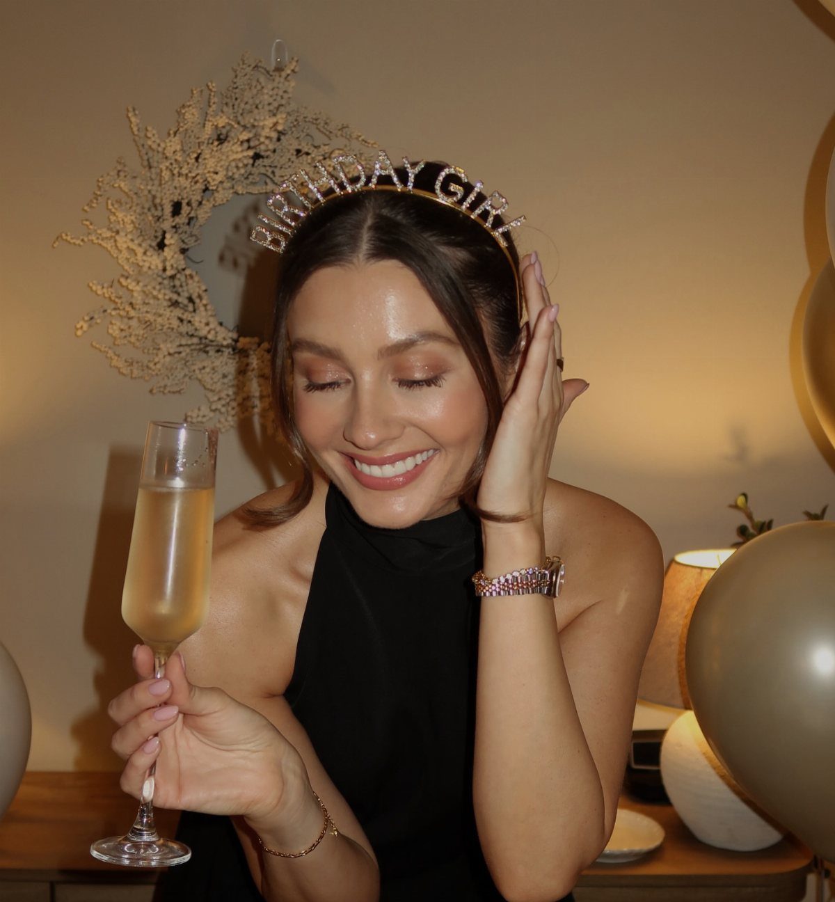 Woman in a black halter dress and birthday headband holding a champagne glass.