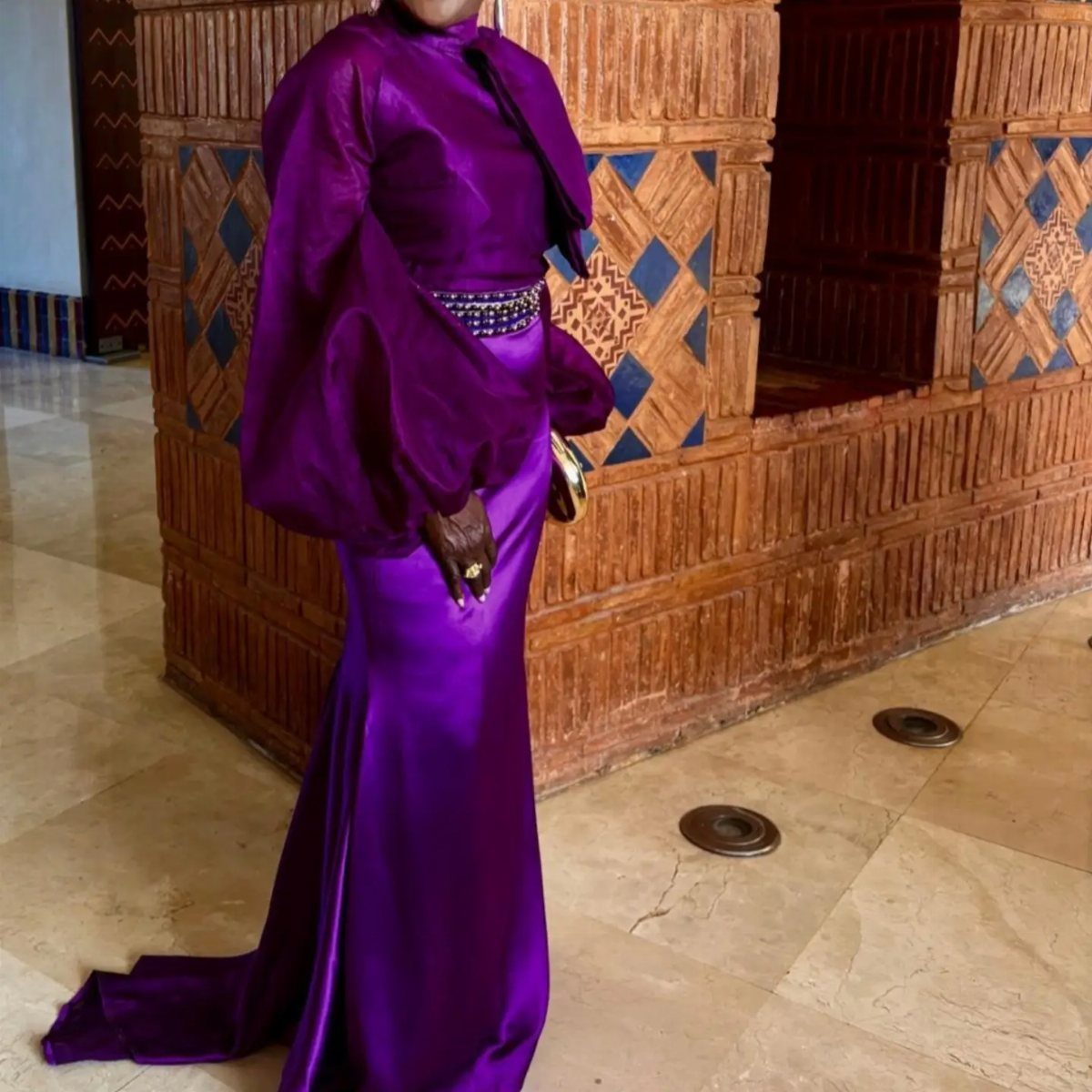 Woman in a shimmering purple satin gown with puffed sleeves and embellished belt.