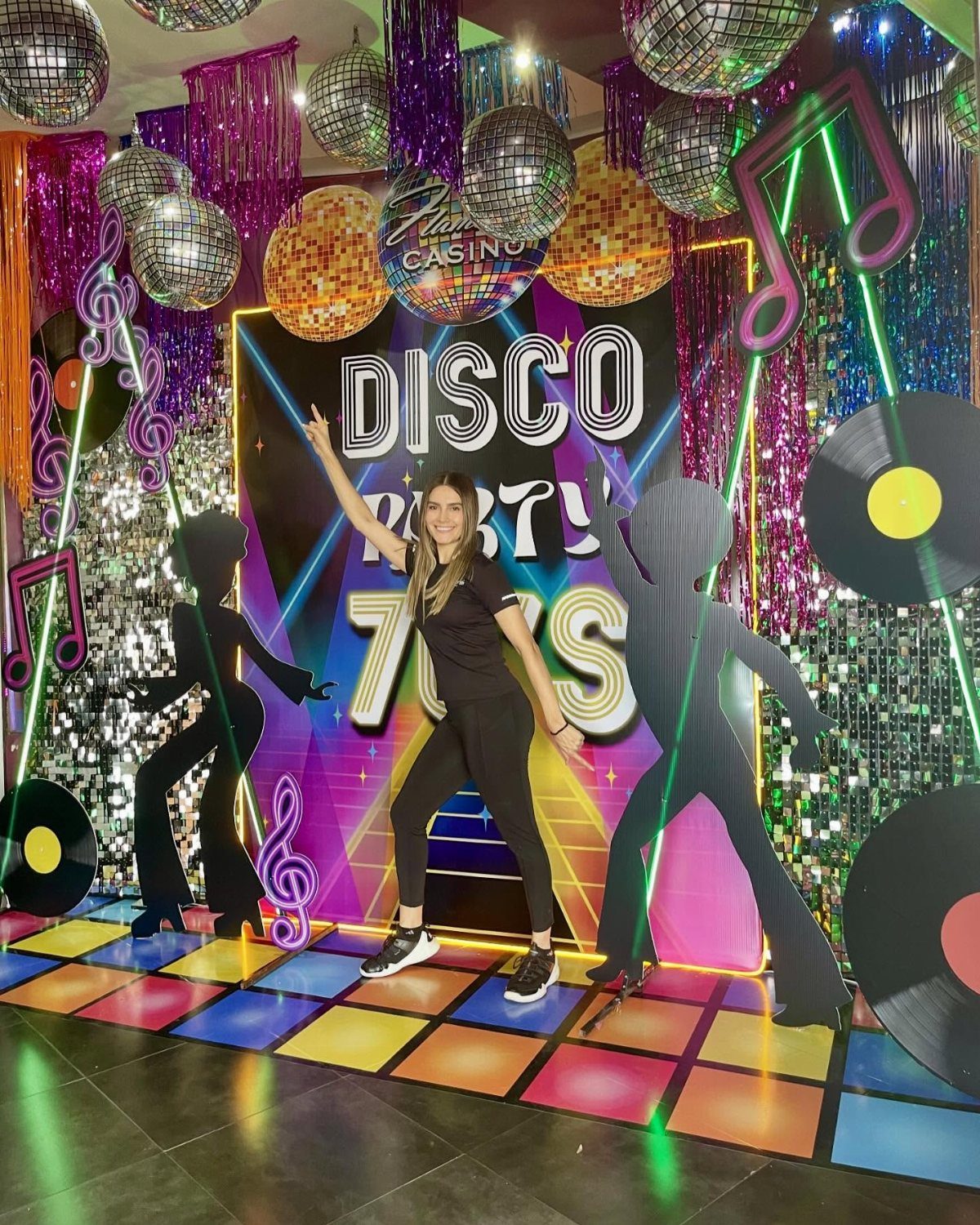 Woman posing on a colorful light-up dance floor with disco party decorations.