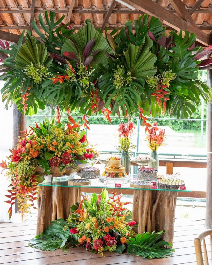 Tropical greenery and vibrant flowers decorating a dessert table with rustic wooden bases.