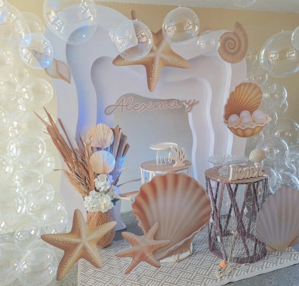 Beach themed party decor with large seashells, starfish, and clear balloons against white backdrop