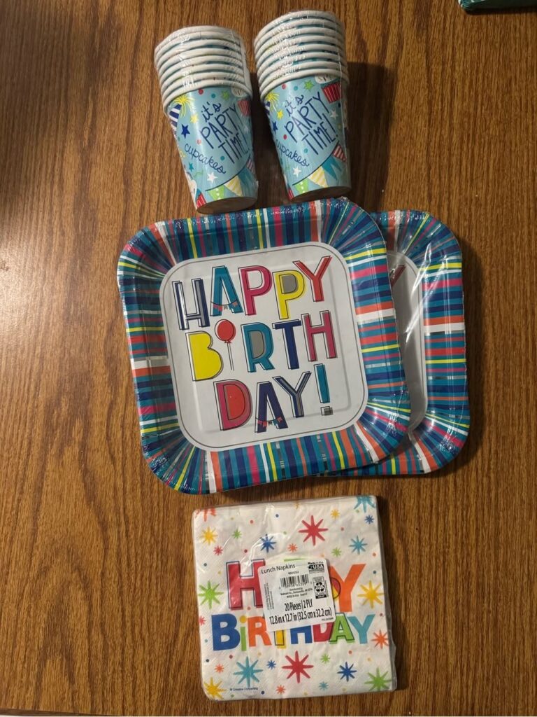 Birthday plates, napkins, and cups arranged on a brown wooden table.