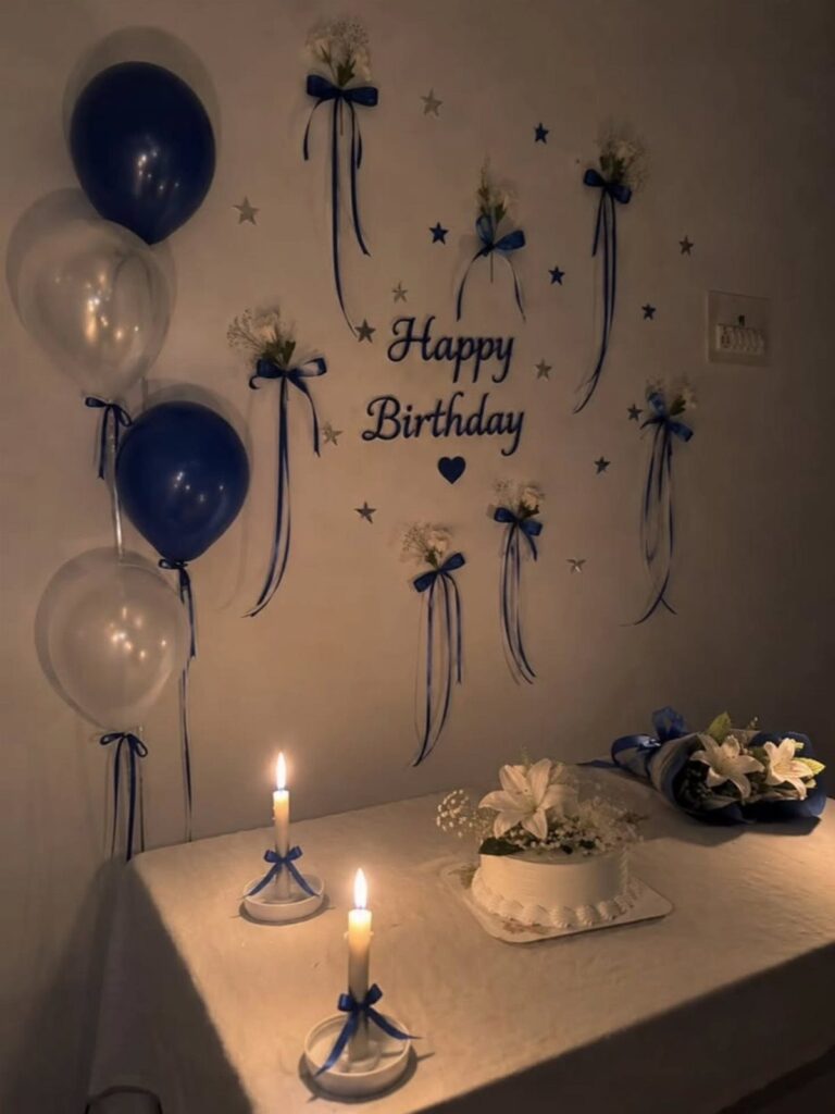 Birthday party home decoration with blue balloons, white cake, and wall ribbons.