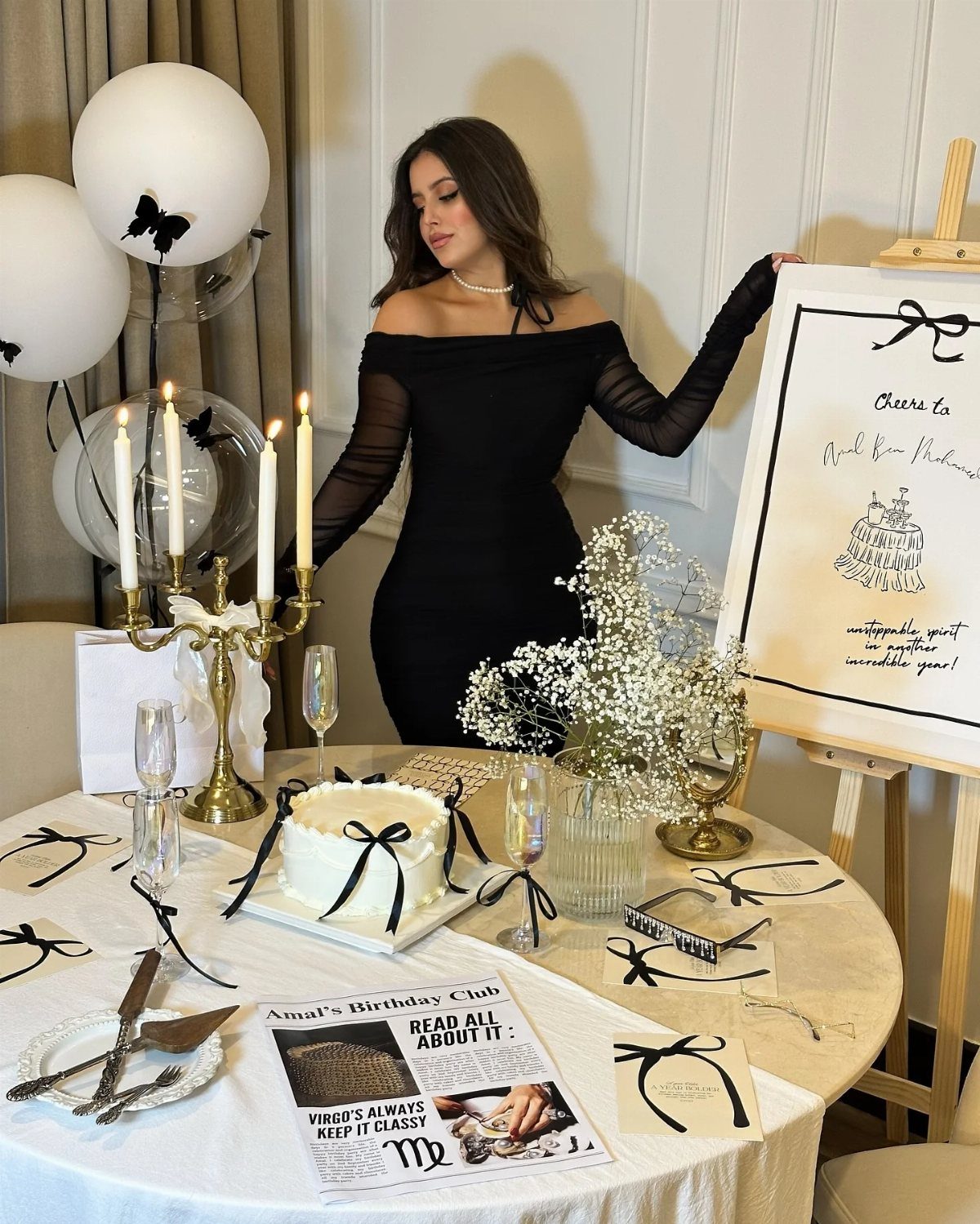 Woman in black dress standing by a black and white themed party table.