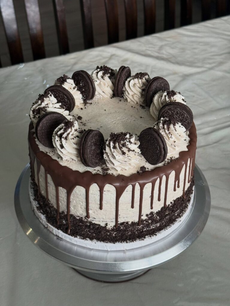 Layer cake with light brown frosting, chocolate drip, and Oreo cookie decorations.