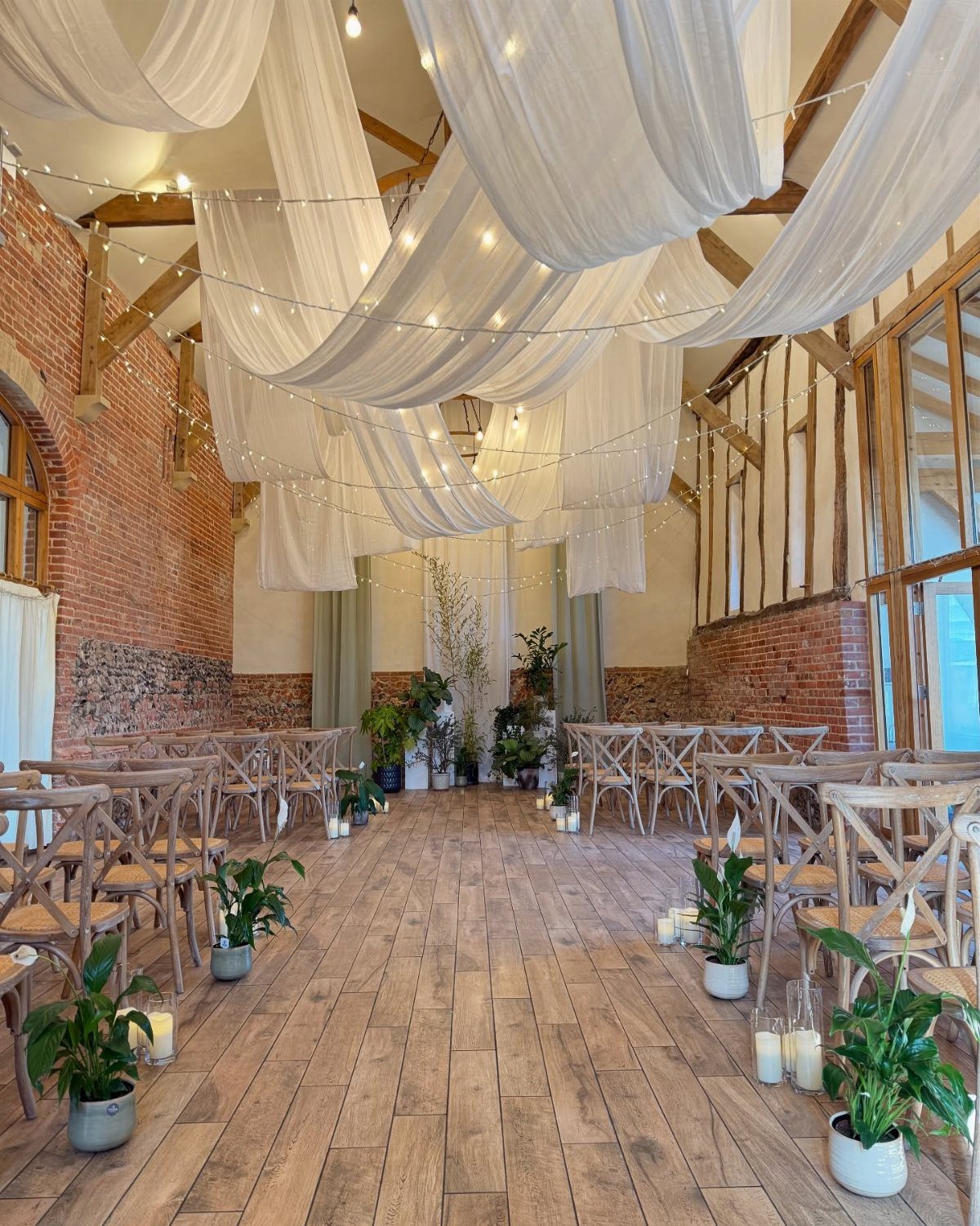 White sheer fabric drapes with fairy lights over a rustic wedding ceremony aisle
