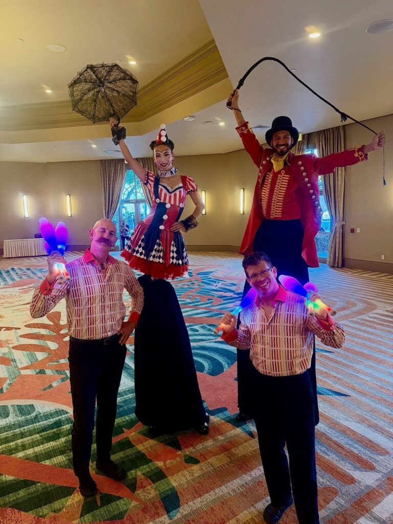 Circus performers including a ringmaster and stilt walker posing in a ballroom.