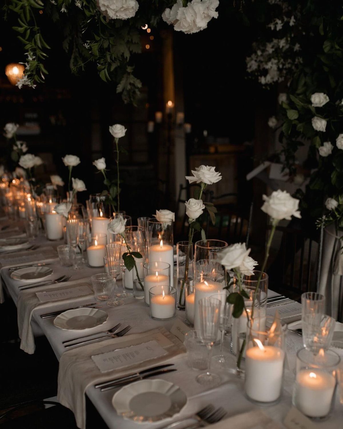 Single white roses in small glass vases and white candles on a wedding table