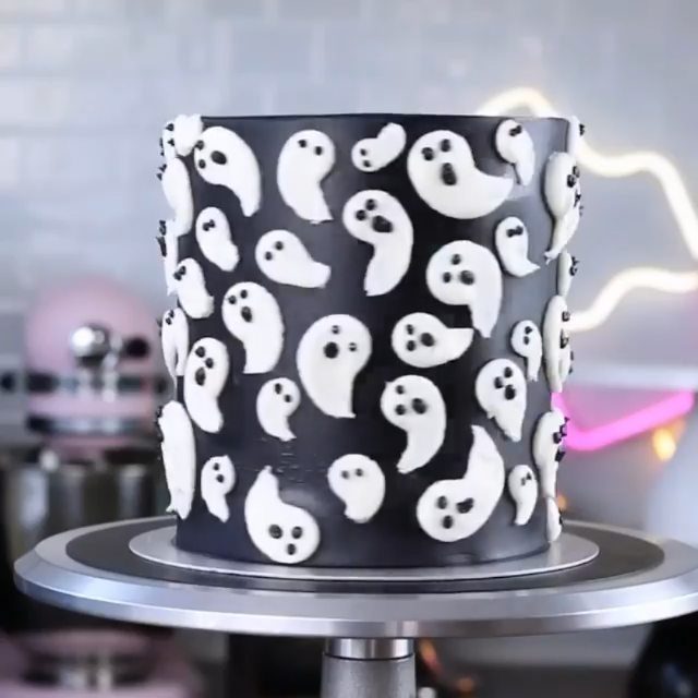 Black frosted cake decorated with white ghost shapes on a silver rotating stand