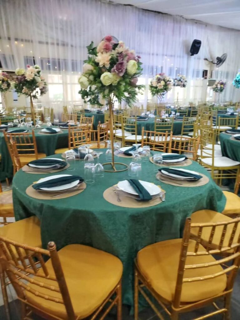 Tall gold flower centerpieces on green tablecloths in a banquet hall setting