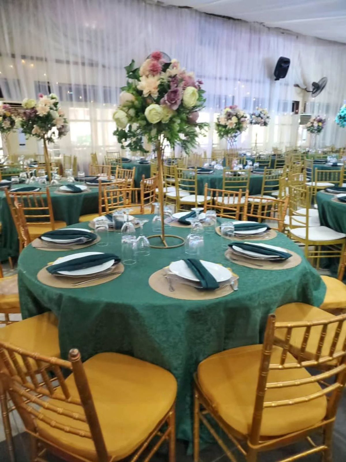 Tall gold flower centerpieces on green tablecloths in a banquet hall setting