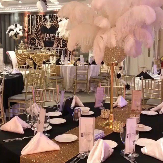 Tall gold centerpiece with fluffy pink and white feathers on a banquet table.