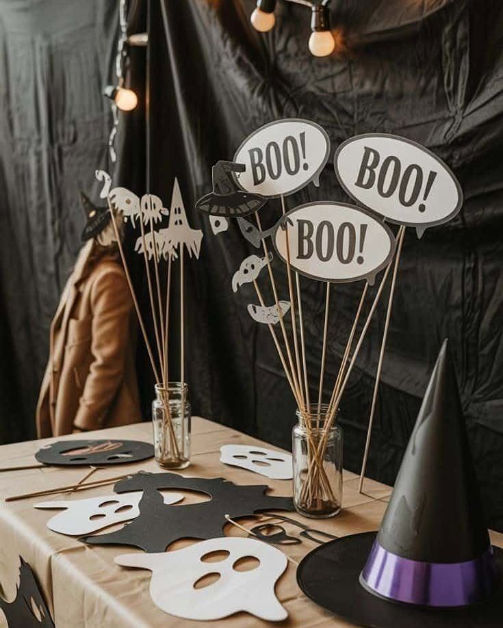 Halloween party decorations with ghost cutouts, BOO signs, and a witch hat on a table.