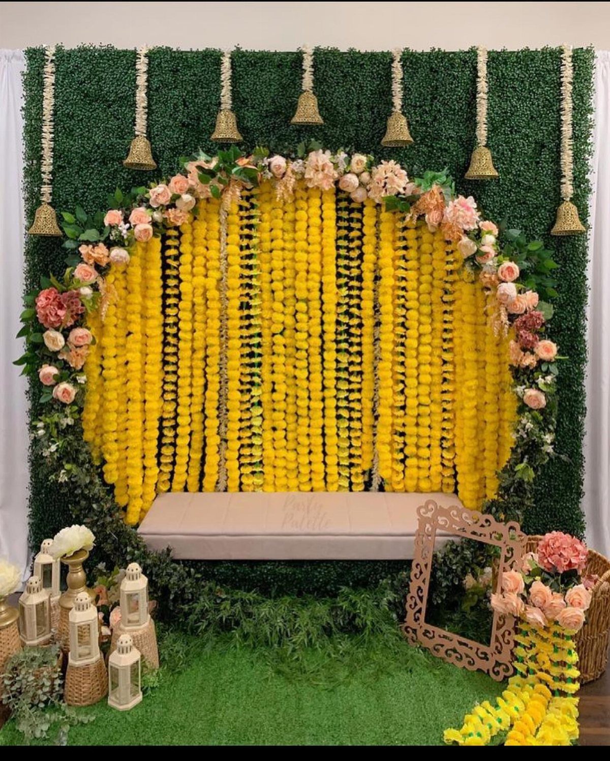 Floral wedding backdrop with yellow garlands, pink roses, and green hedge wall.