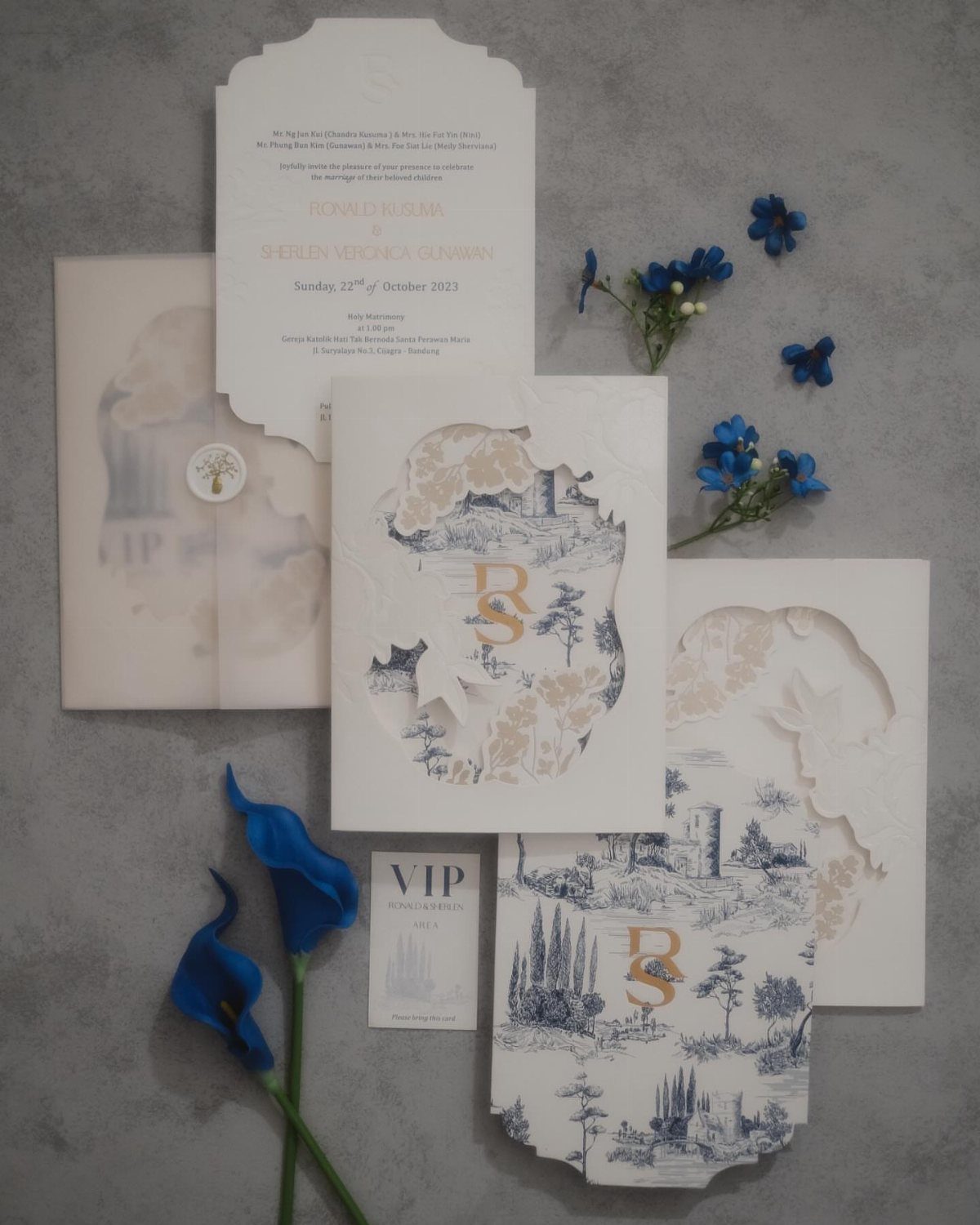 Laser cut wedding invitations with blue landscape illustrations and blue flowers on grey background