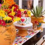 Festive Mexican party decorations with colorful flowers, a decorated cake, and embroidered runner.