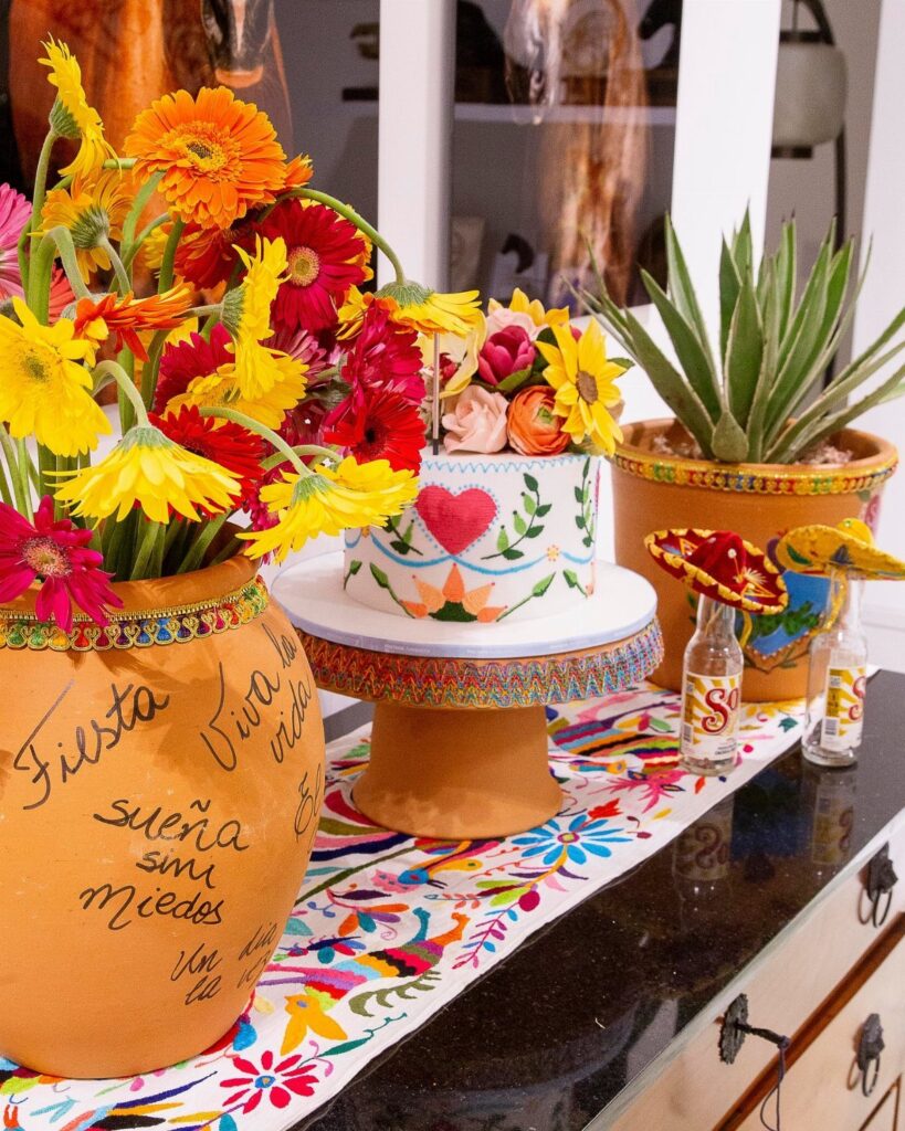 Festive Mexican party decorations with colorful flowers, a decorated cake, and embroidered runner.