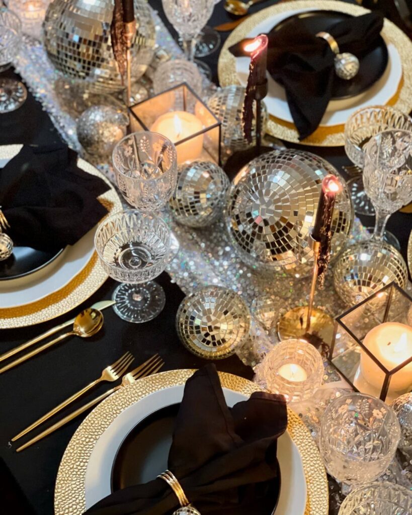 Festive dining table with black and gold settings, disco balls, and lit candles.