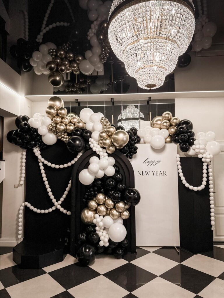 New Year's party decor with black, white, and gold balloons on checkered flooring.