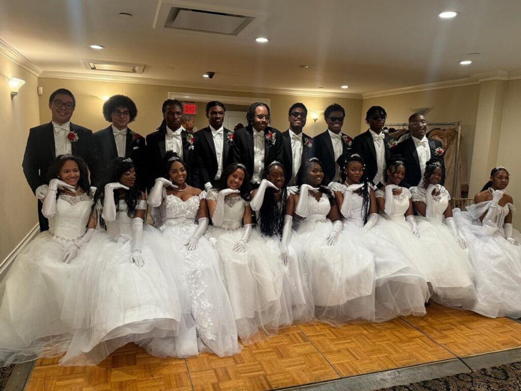 Group of young adults in black tuxedos and white ball gowns posing together.