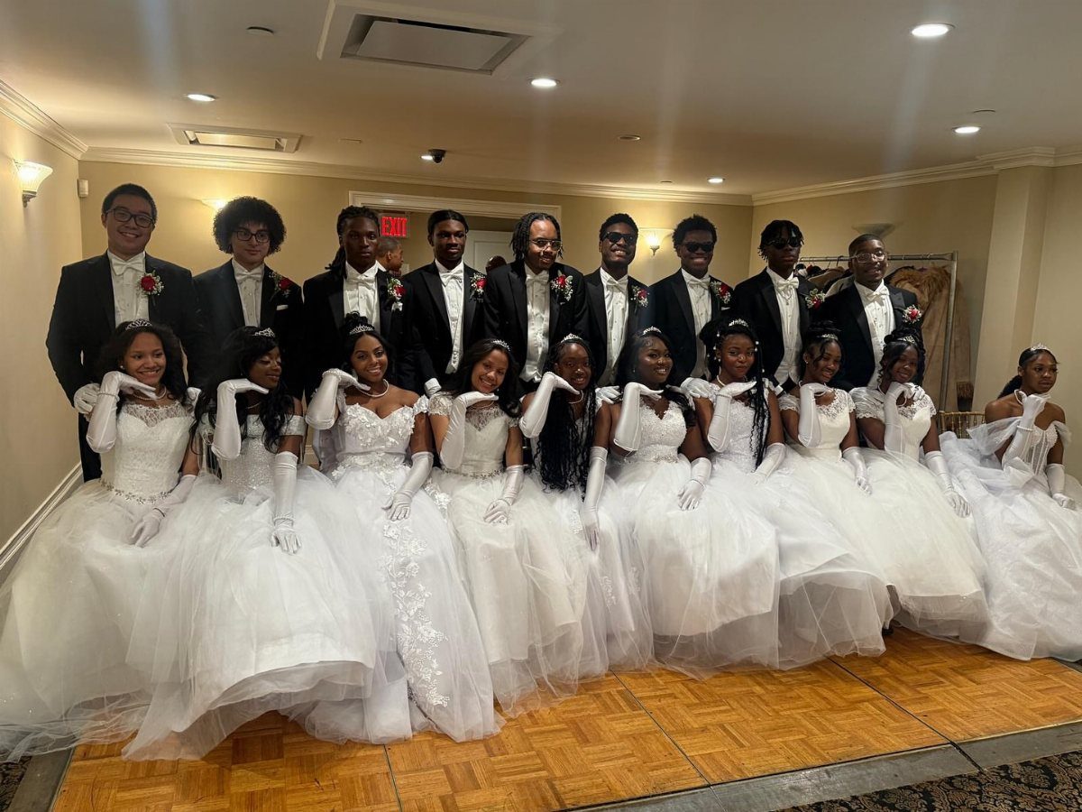 Group of young adults in black tuxedos and white ball gowns posing together.