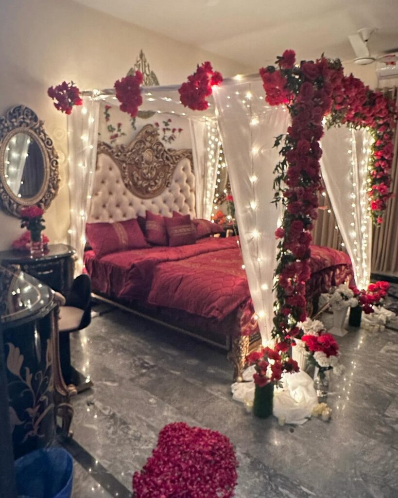 Wedding decorated bedroom with red linens, white canopy, fairy lights, and red roses.