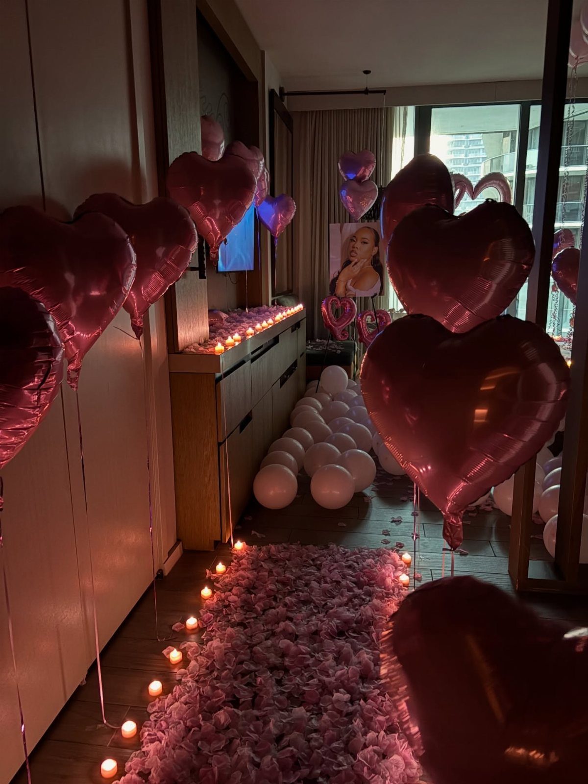 Pink heart-shaped balloons and white balloons decorating a room with flower petals.