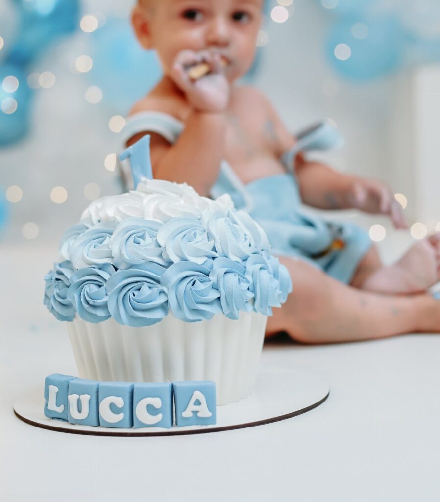 Small white cake with blue frosting swirls and blue letter blocks spelling LUCCA.