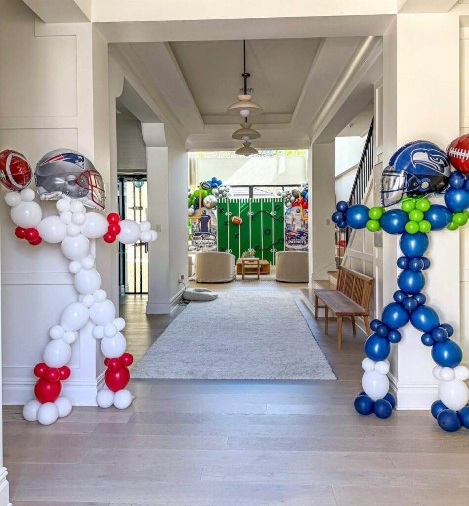 Balloon sculptures shaped like football players wearing helmets in a decorated white hallway.