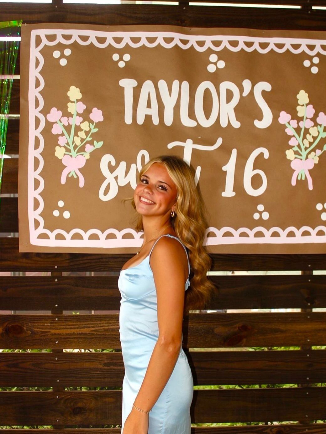 Teenage girl in a light blue satin dress posing before a sweet 16 banner