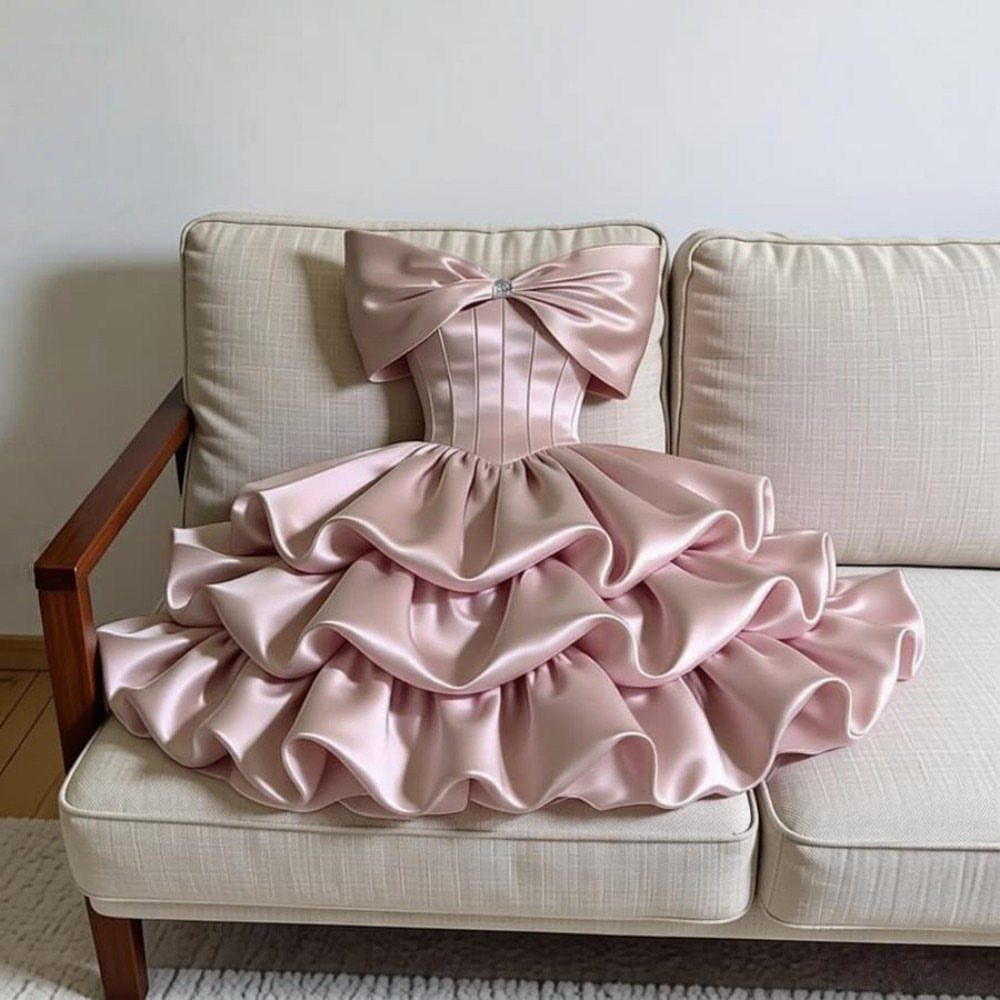 Pale pink satin ballgown with tiered ruffles and bow neckline on a beige sofa