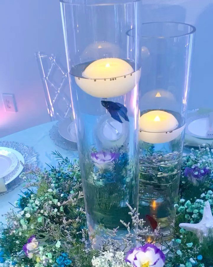 Glass cylinder centerpieces with floating candles, blue fish, and surrounding blue floral arrangements.