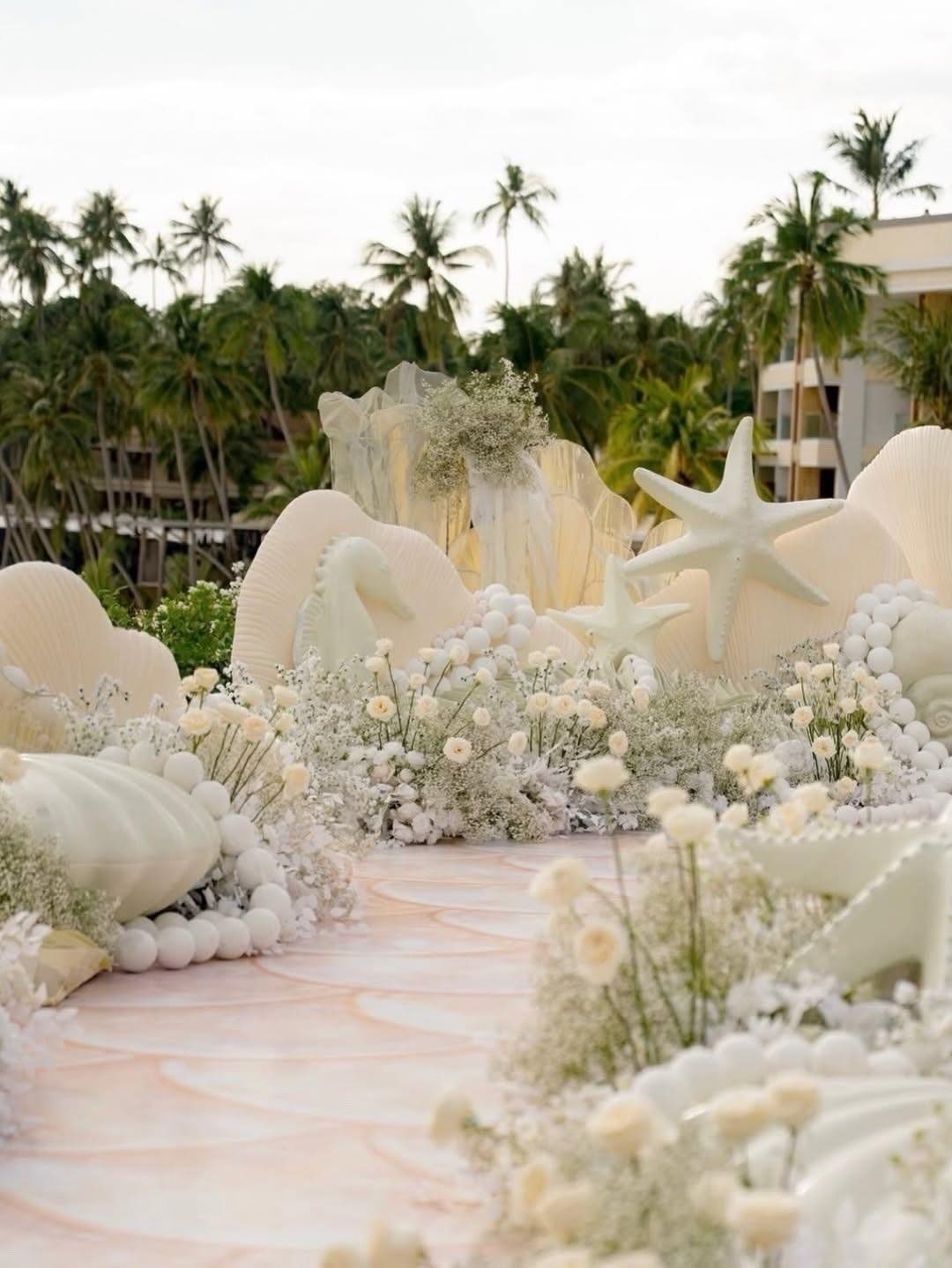 Wedding aisle decorated with giant white seashells, starfish, and white flowers on a beach.