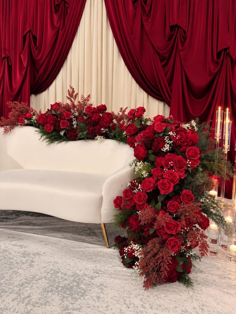 White curved sofa decorated with red roses against red and cream draped curtains.