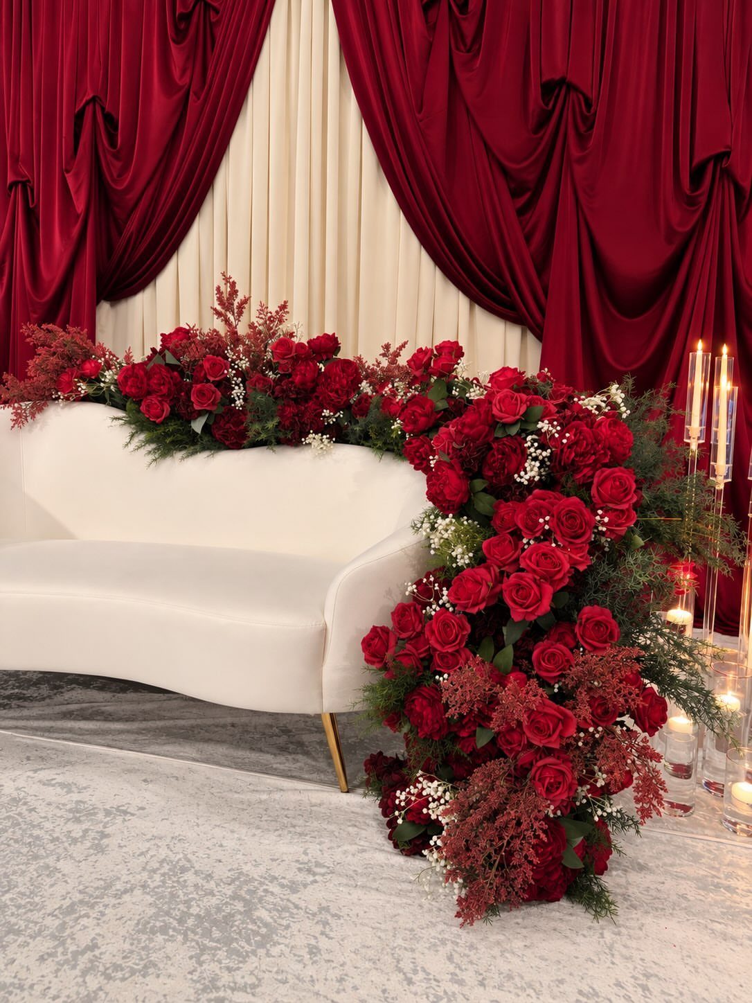 White curved sofa decorated with red roses against red and cream draped curtains.